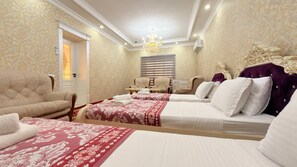 Habitación de hotel con dos camas, zona de estar con sillones, candelabro y un ventanal con persianas.