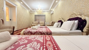 A hotel room with two beds, a chandelier, a large window with blinds, and a red carpet.