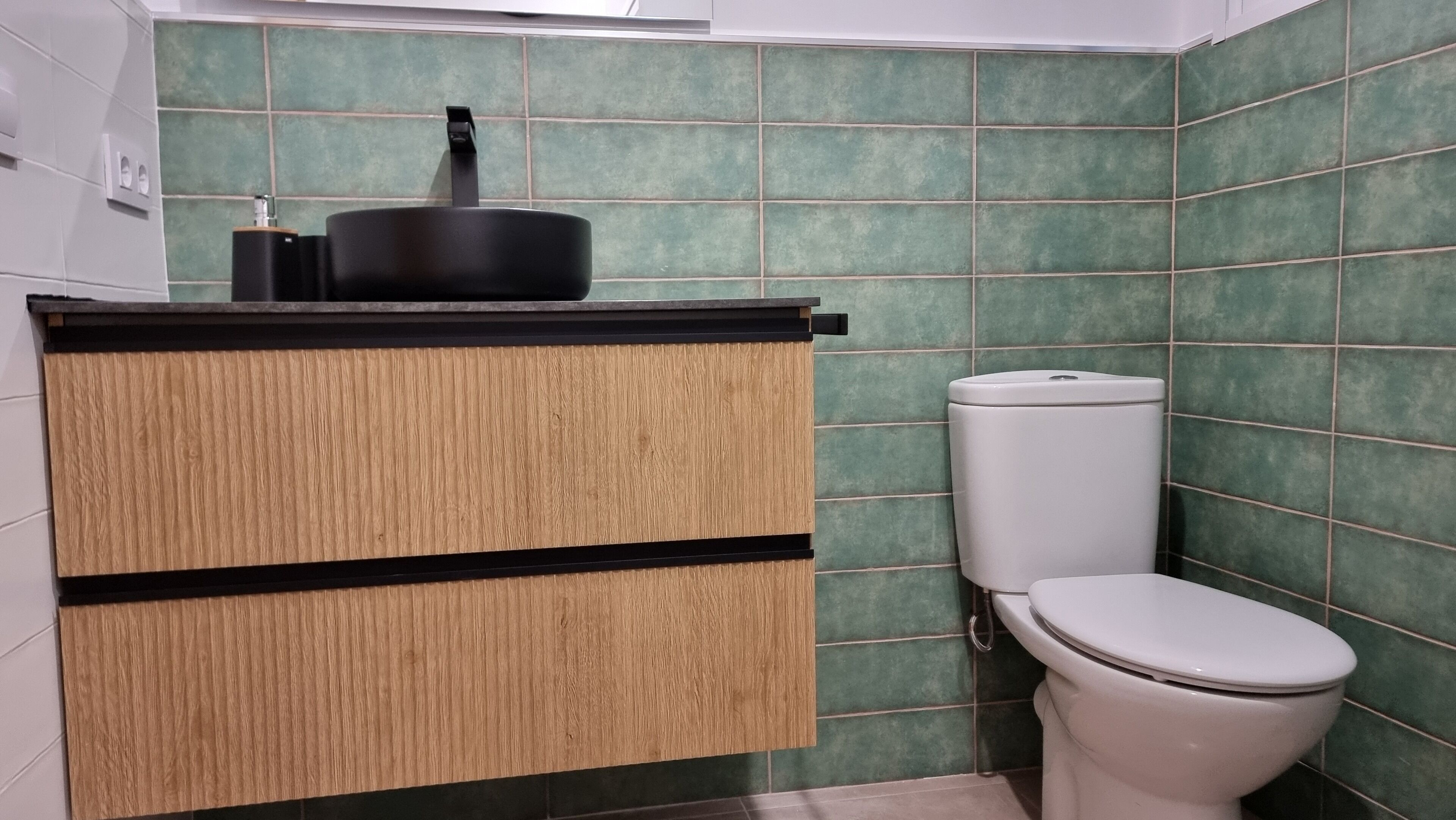A bathroom with a toilet, a sink with a black faucet, and a cabinet with a wooden finish.
