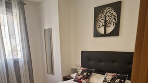 Een net opgemaakt bed met een beige sprei, twee kussens met bloemenmotieven en twee gevouwen handdoeken op het bed.