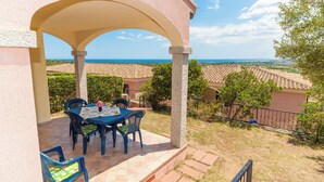 A covered outdoor seating area with a table and chairs, overlooking a scenic landscape with buildings and the sea. - Apartments with spectacular views of Budoni Bay 3 min. from the sea-4 places (Malamurì)