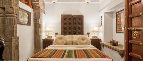 A bedroom with a large bed, two bedside lamps, a wooden door, and a stone wall with carvings.