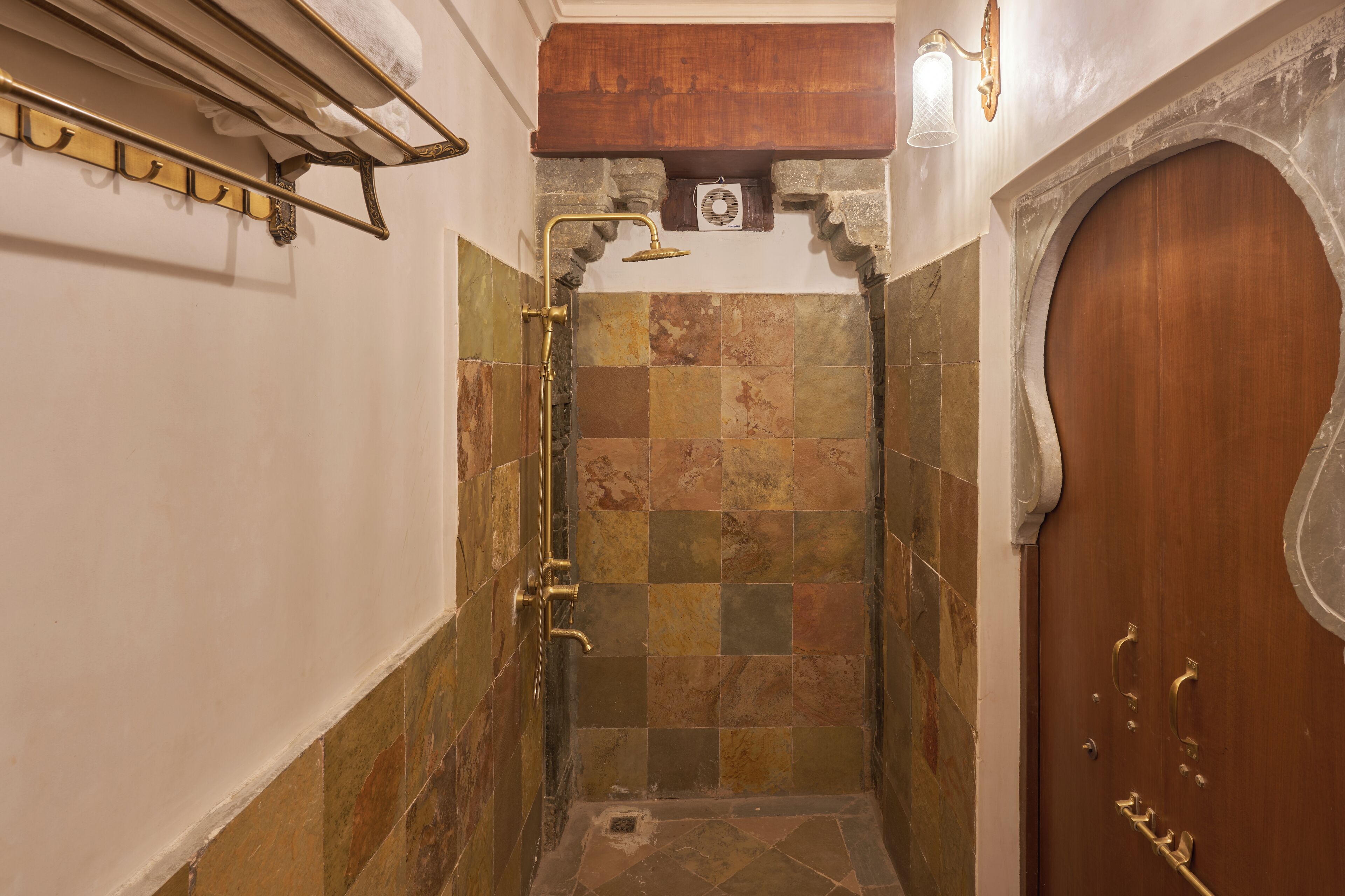 A bathroom with a shower, tiled walls, a wooden door, and a towel rack.