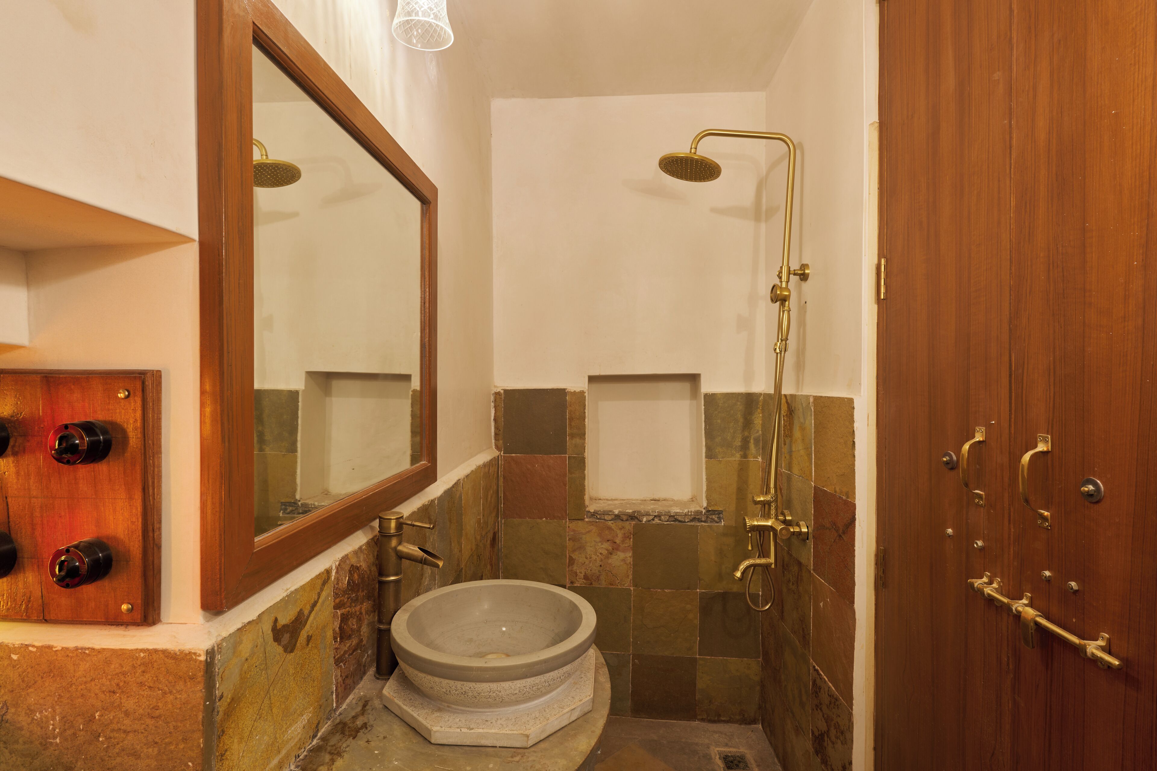 Une salle de bain avec un lavabo en pierre, un miroir, une douche et une porte en bois.