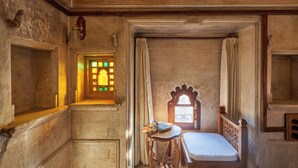 A small, rustic room with a wooden bed, a small table, and a window with curtains. - Kaladwas Lal Haveli (Udaipur)