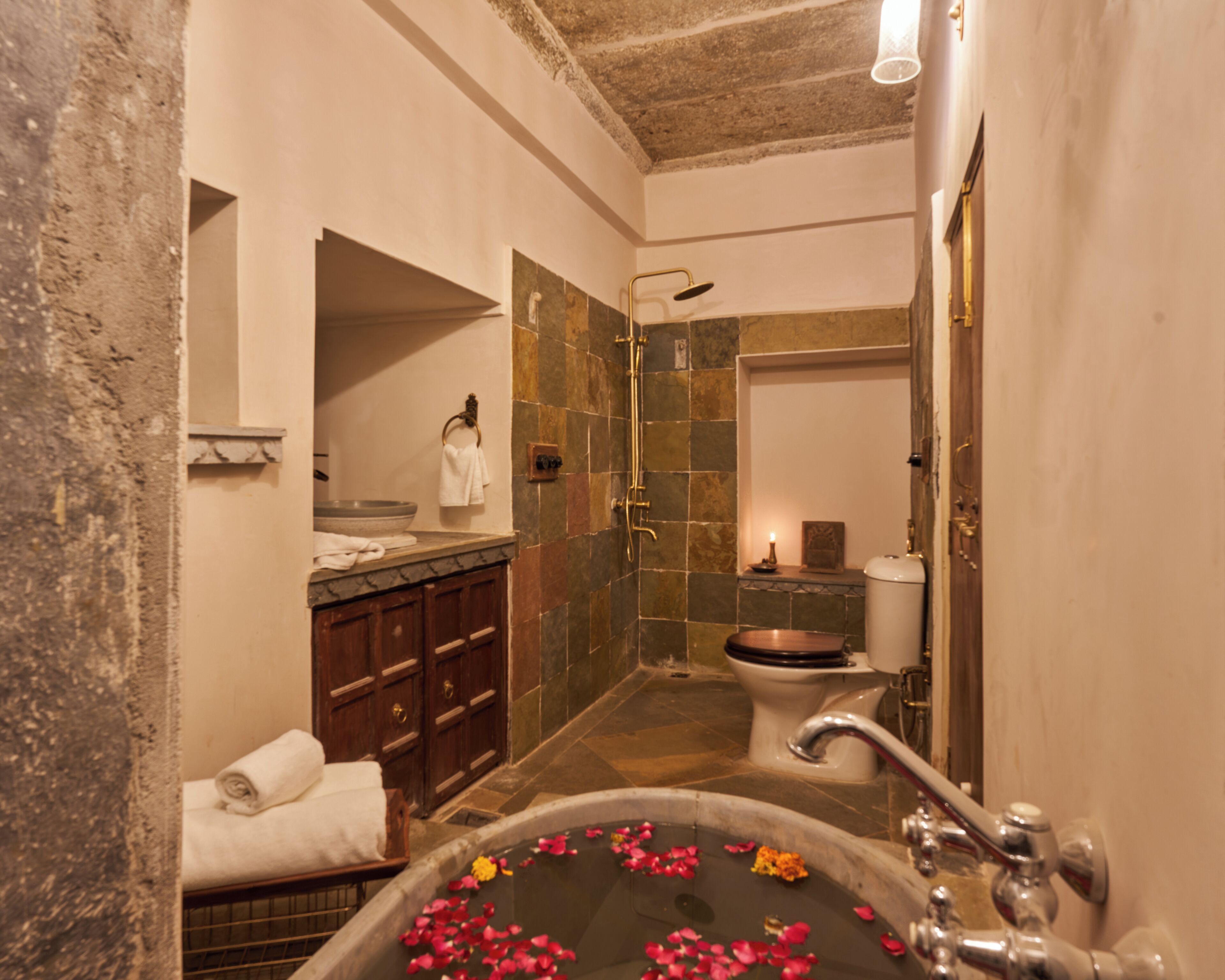 A bathroom with a bathtub filled with rose petals, a shower, a toilet, and a vanity with a basin and towel rack.
