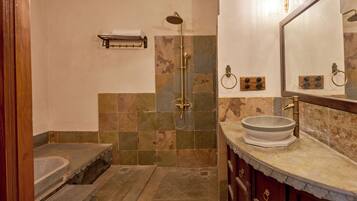 Un baño con ducha de piedra, lavabo y espejo con marco de madera.