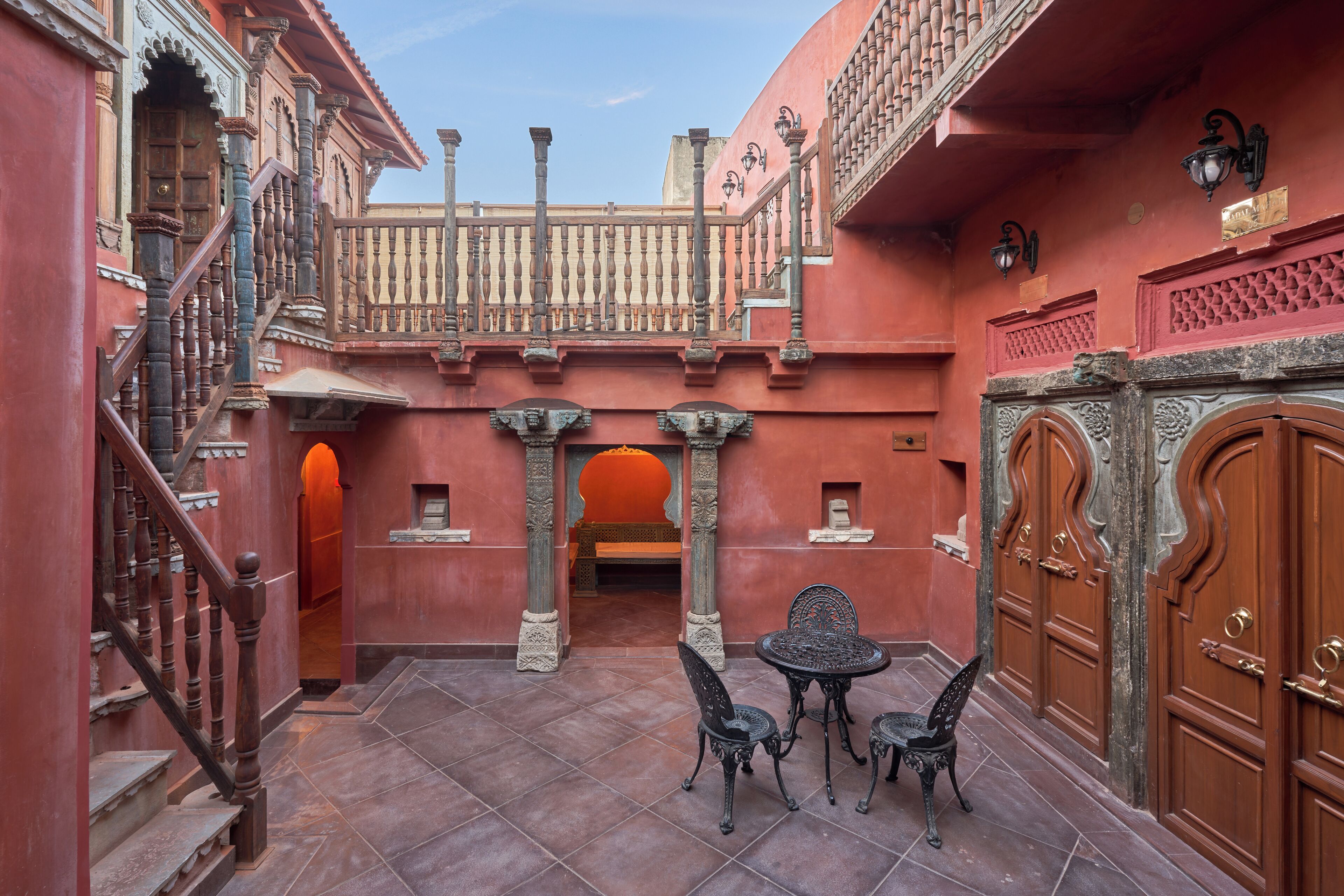 A courtyard with a staircase, a table with chairs, and ornate doors.