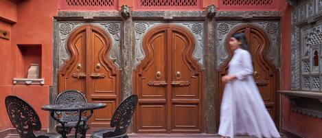A courtyard with ornate wooden doors, a round table, and metal chairs.