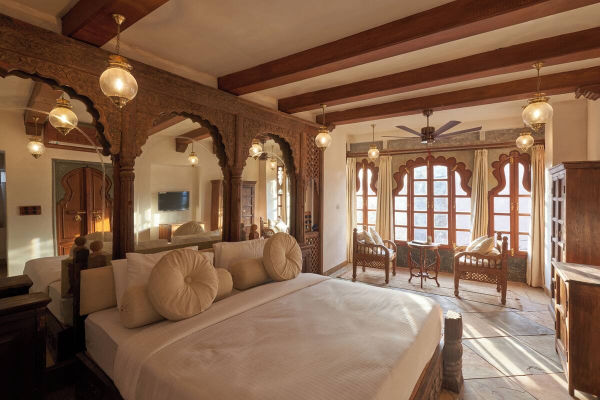 A spacious bedroom with a large bed, wooden beams, and ornate ceiling details.