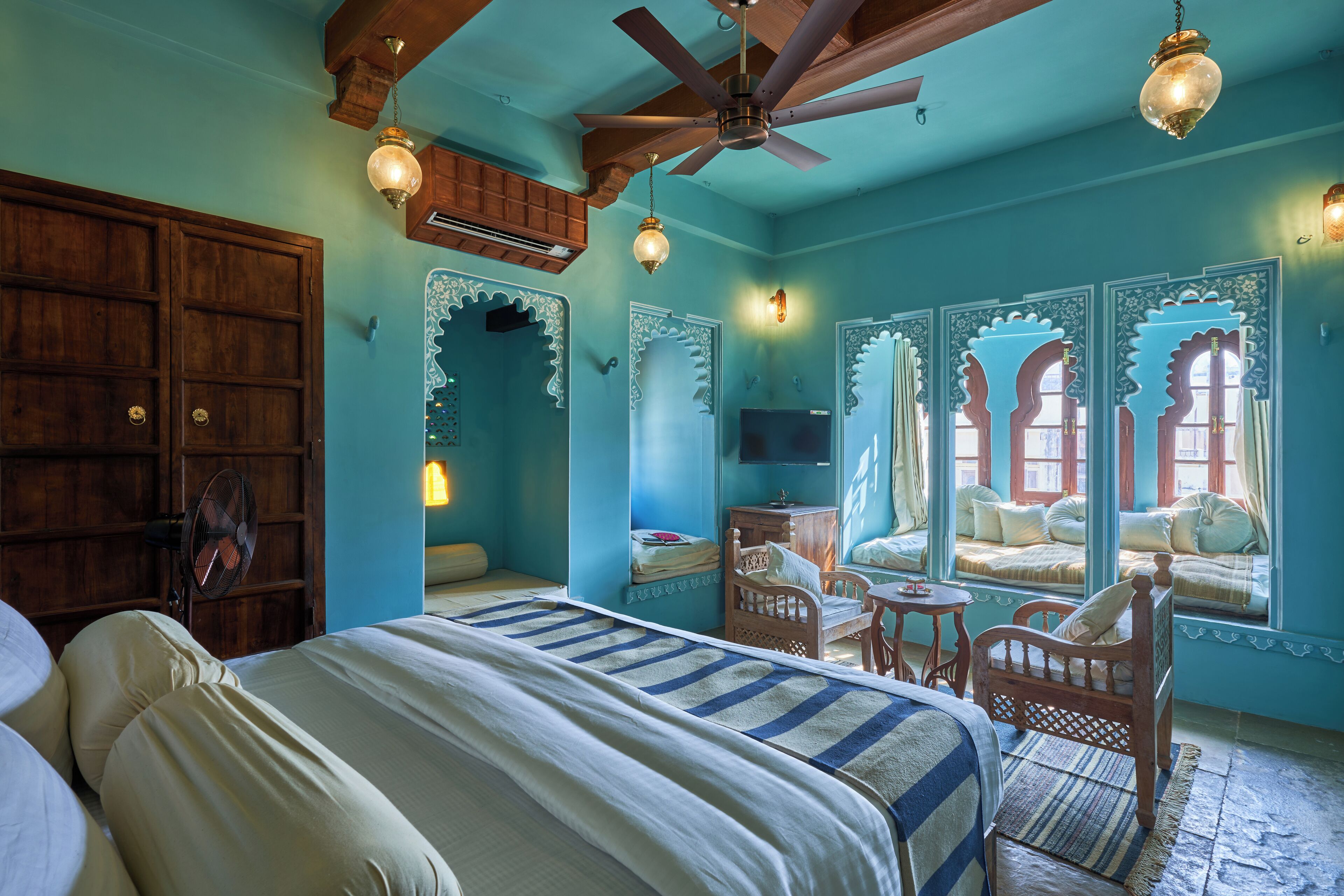 A room with a bed, wooden furniture, a ceiling fan, and a window seat with cushions.