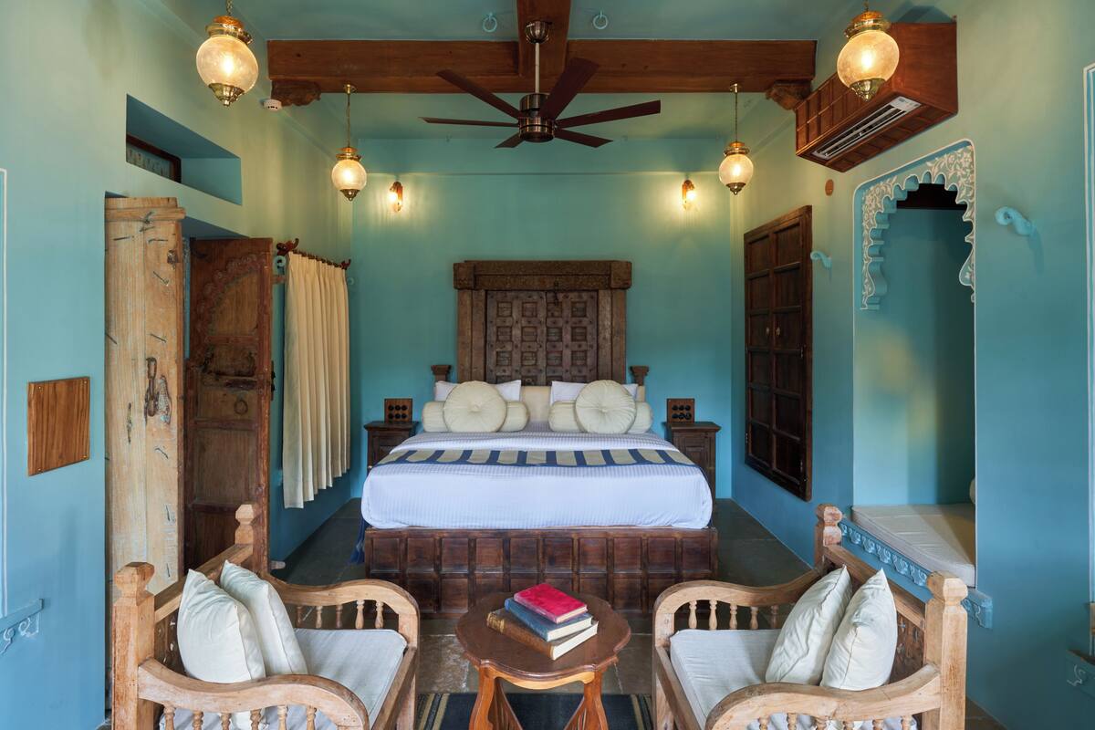 A bedroom with a large bed, two wooden chairs, a small table, and a ceiling fan.