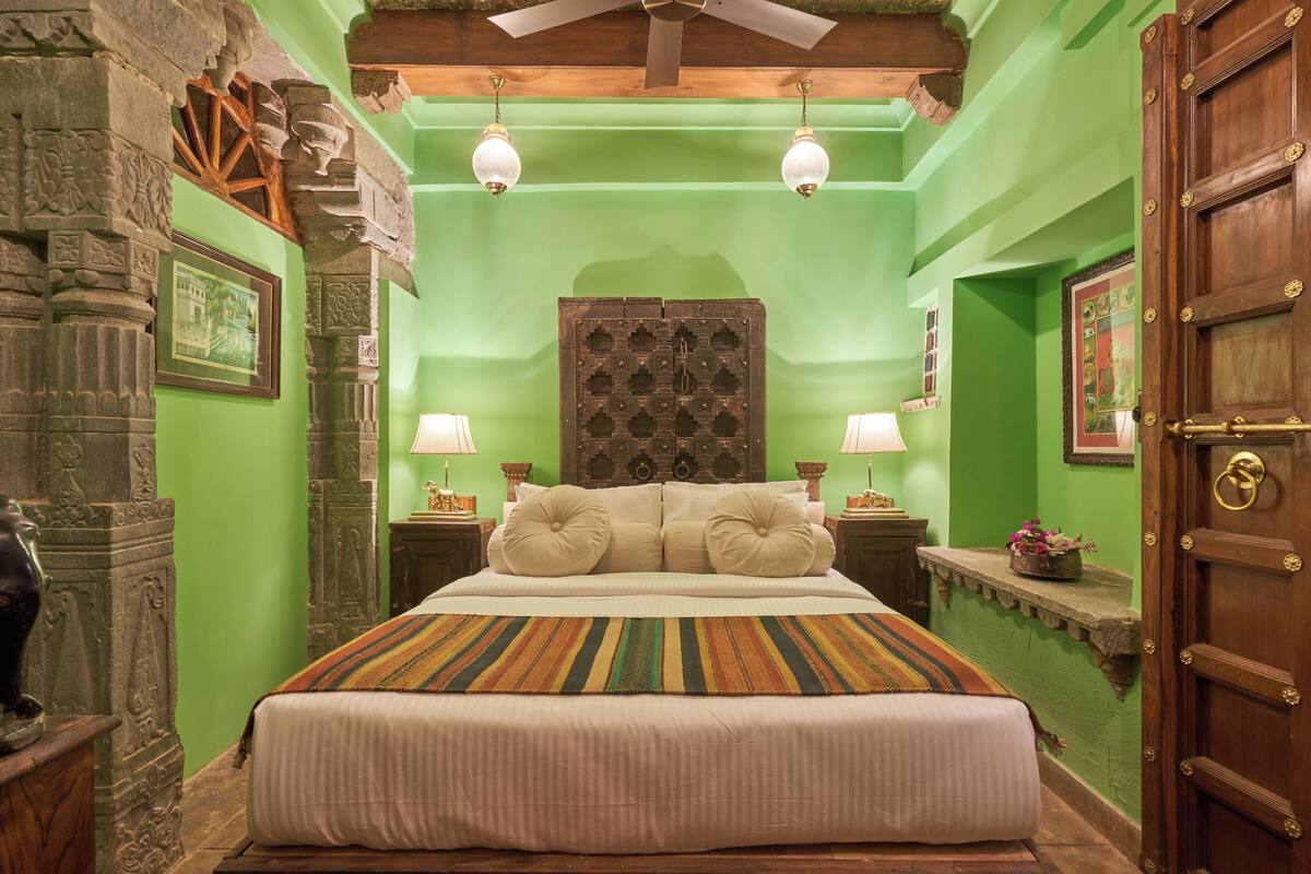 A room with a large bed, green walls, wooden door, and a ceiling fan.