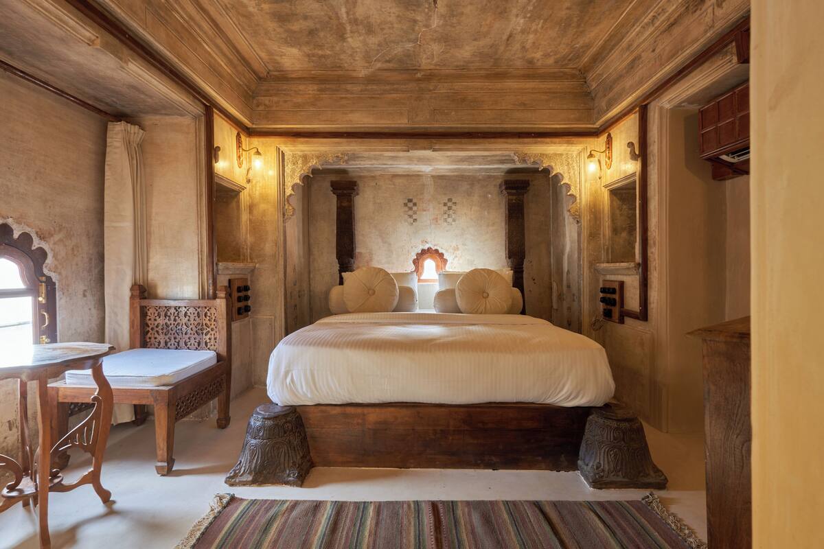 A traditional room with a large bed, a wooden desk, and a small table.