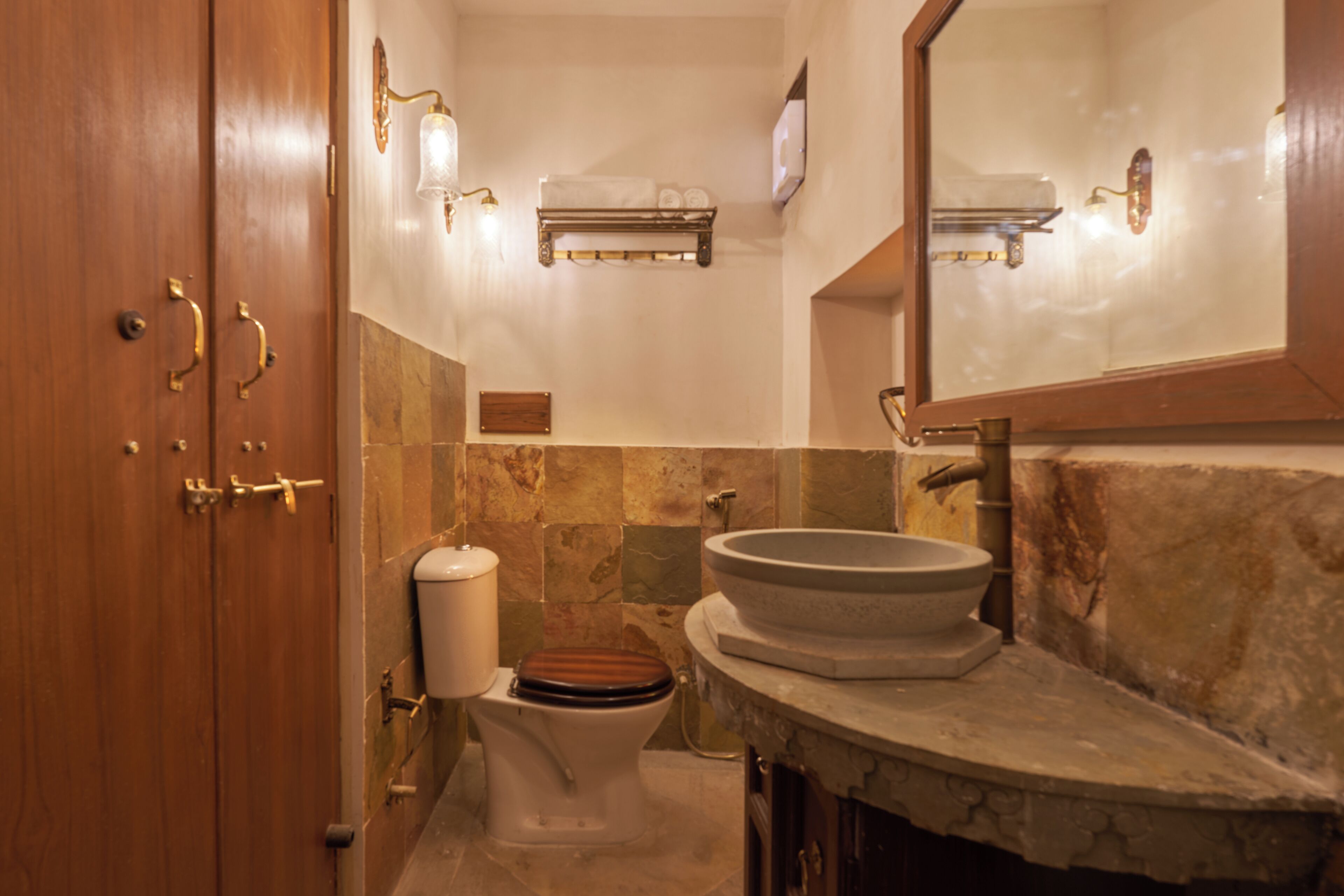 Ein Badezimmer mit Holztür, Toilette mit Holzsitz, Waschbecken mit Natursteinplatte und Spiegel über dem Waschbecken.