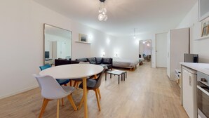 A modern living room with a sofa, a dining table with chairs, a TV, and a kitchen area with a refrigerator. - Fully-equipped apartment Vieux Lyon (Lyon)