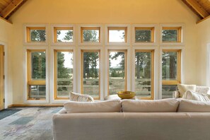 A room with a large window, a beige sofa, and a yellow bowl on a table.