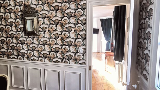 Une pièce avec un papier peint à motifs floraux, un miroir et un plancher en bois.