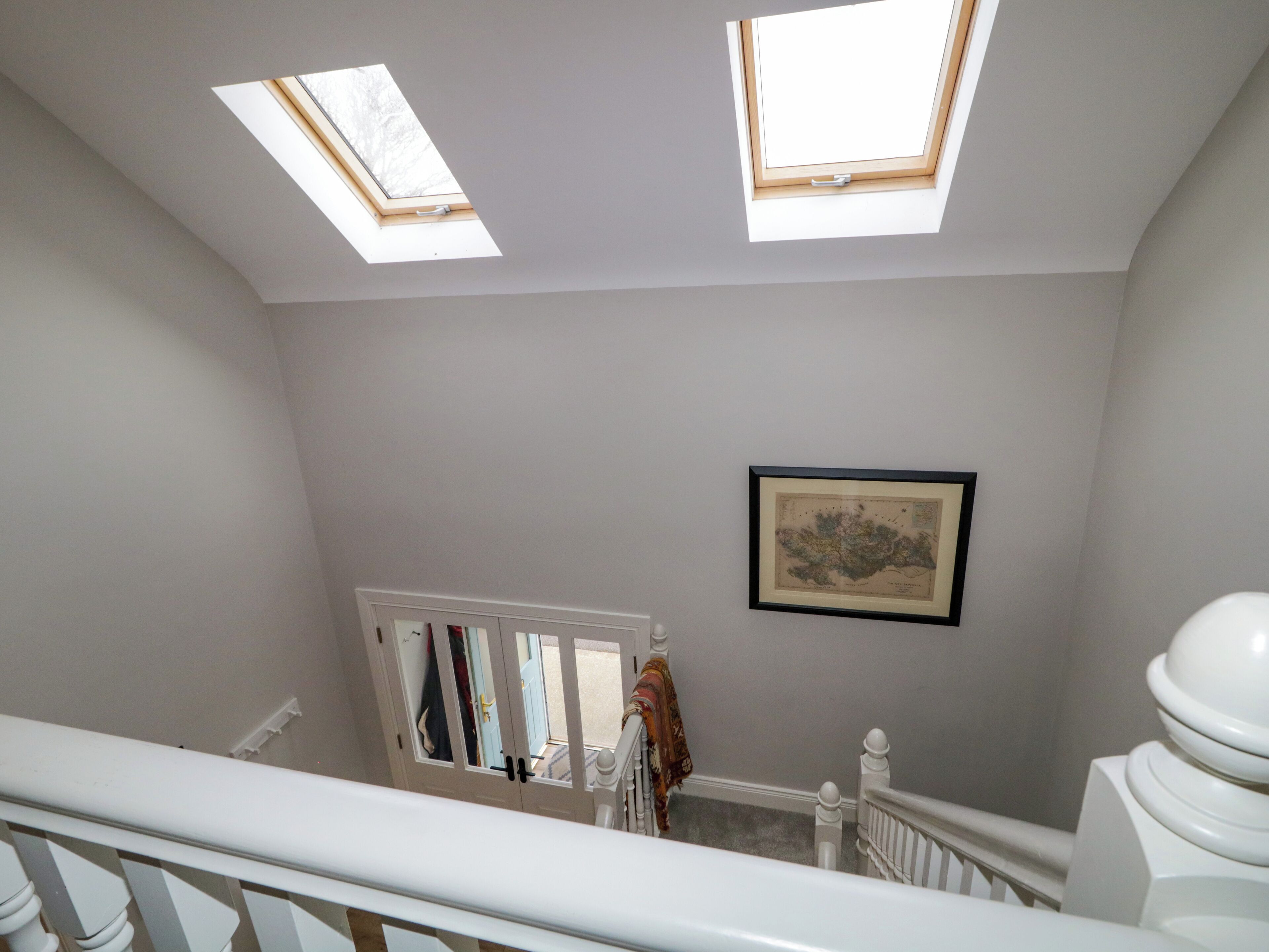 Un intérieur spacieux avec un plafond haut, des fenêtres de toit, un escalier et une carte encadrée accrochée au mur.