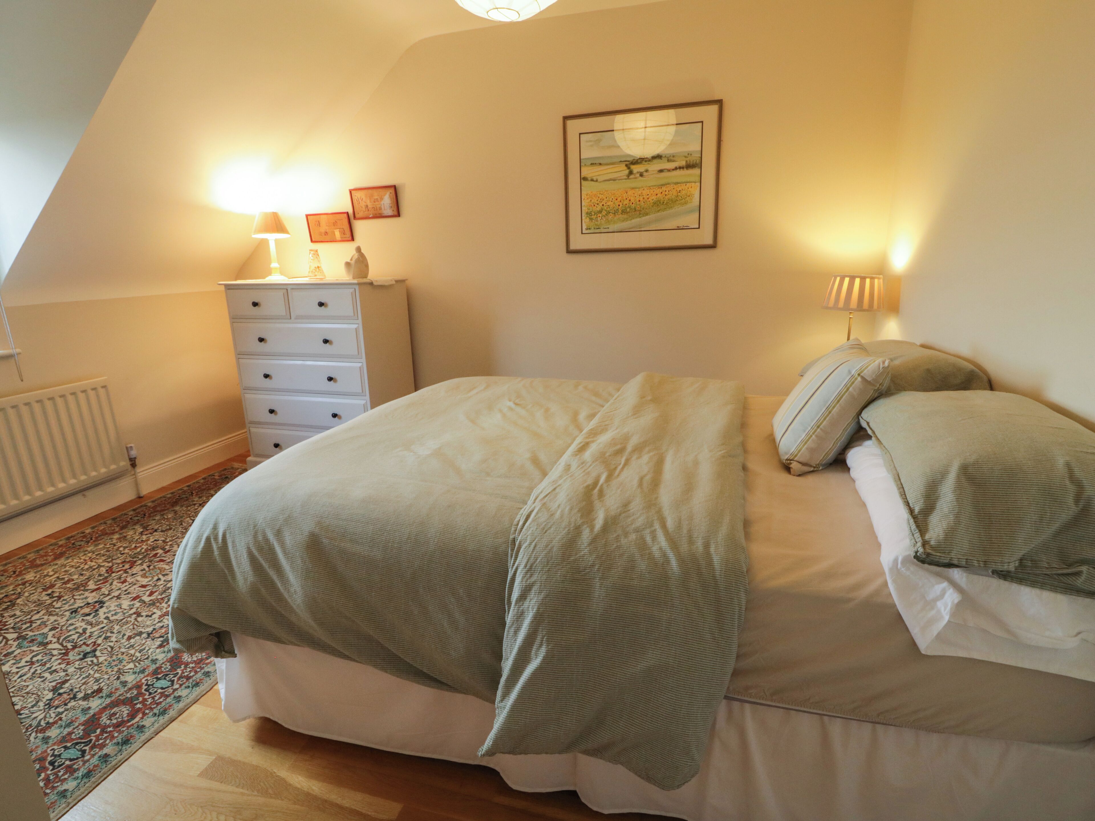 A bedroom with a bed, a dresser, a radiator, a rug, and a painting on the wall.