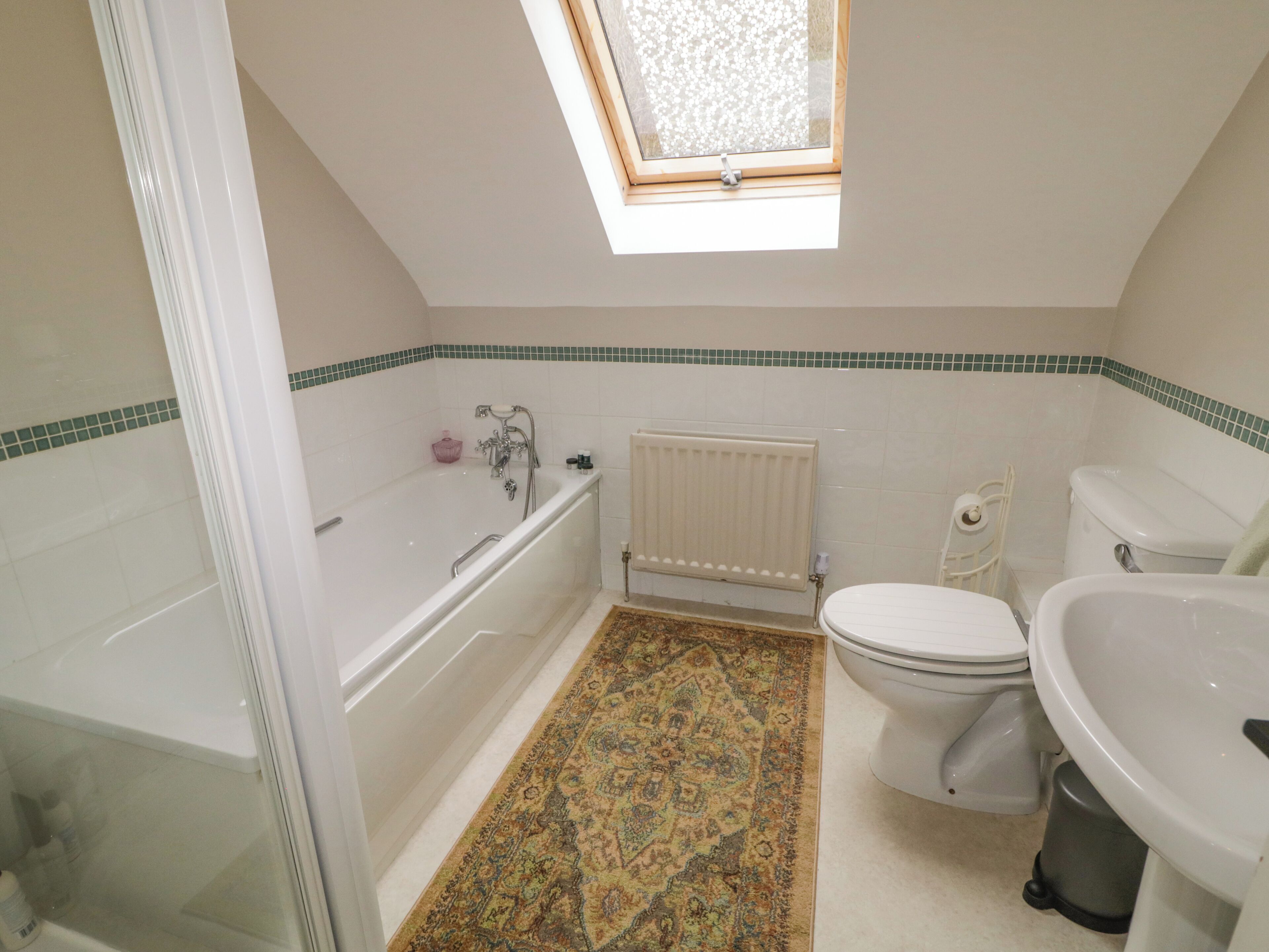 Un bagno con vasca, WC e lavandino, dotato di un lucernario e pavimento decorato.