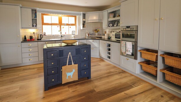Una cucina moderna con mobili bianchi, un'isola centrale e un pavimento in legno.