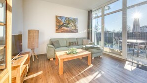 Un salón amplio con un gran ventanal, una mesa de centro de madera, un sofá verde y un cuadro en la pared.
