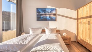 Un dormitorio con una cama grande, un armario de madera, una mesita de noche y un cuadro con un atardecer sobre un cuerpo de agua.