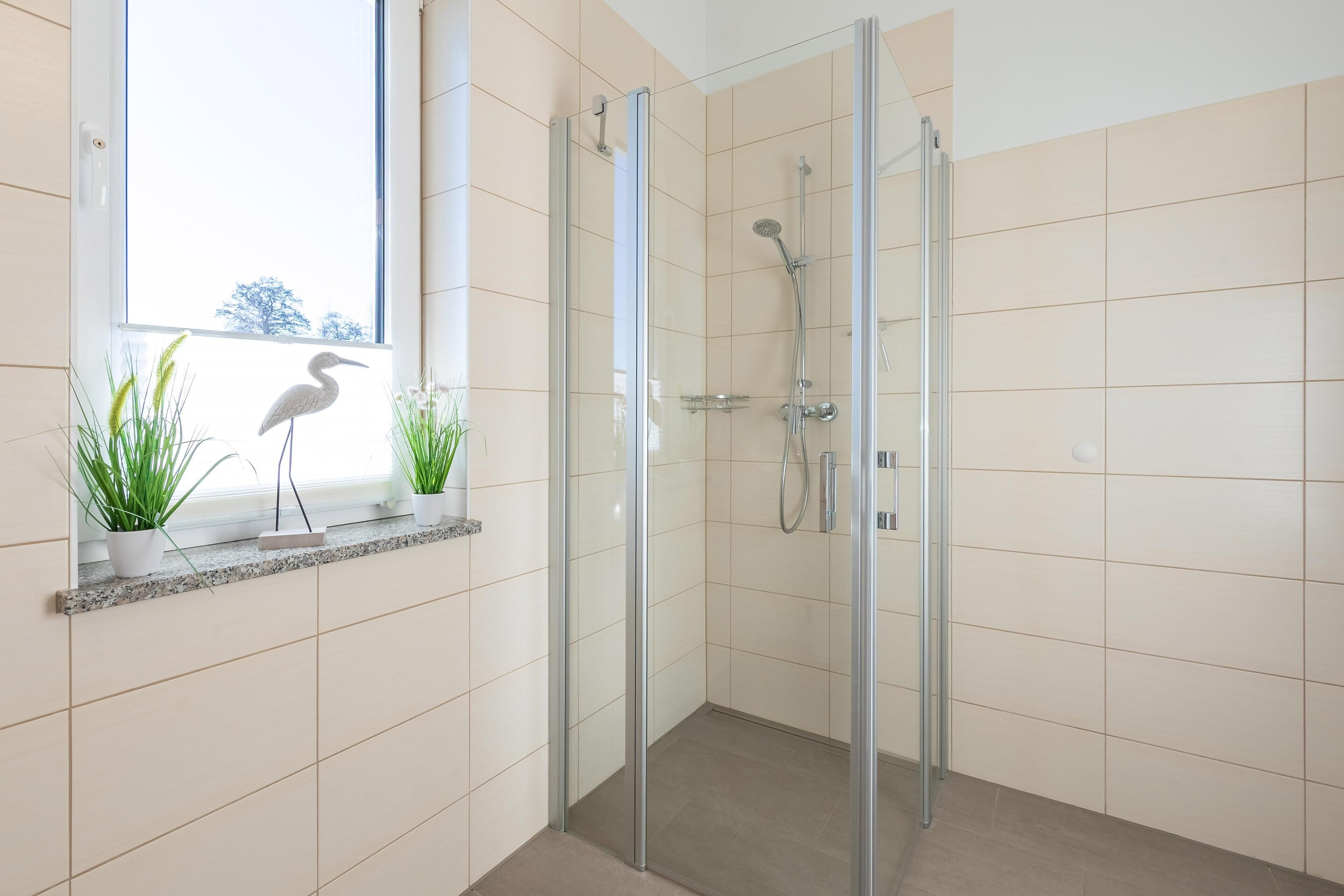 Een moderne badkamer met een douchecabine van glas, een raam met planten en uitzicht op bomen.