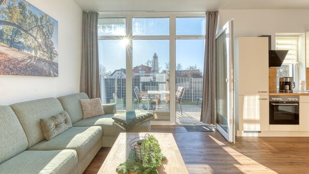 Un apartamento moderno con sala de estar, cocina y amplias puertas correderas de vidrio hacia un balcón.