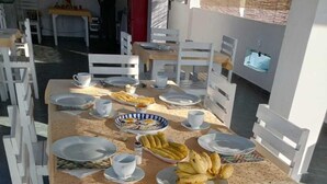 Ruokapöytä on katettu lautasilla, kulhoilla ja aterimilla, ja sen ympärillä on valkoisia tuoleja.