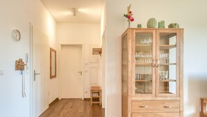 A hallway with wooden flooring, a cabinet with glass doors, and a clock on the wall.