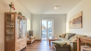 A spacious living room with a wooden cabinet, a green sofa, a wooden coffee table, and a painting on the wall.