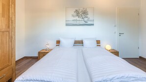 A double bed with white bedding, two bedside tables with lamps, a wooden wardrobe, and a wall-mounted picture of a tree.