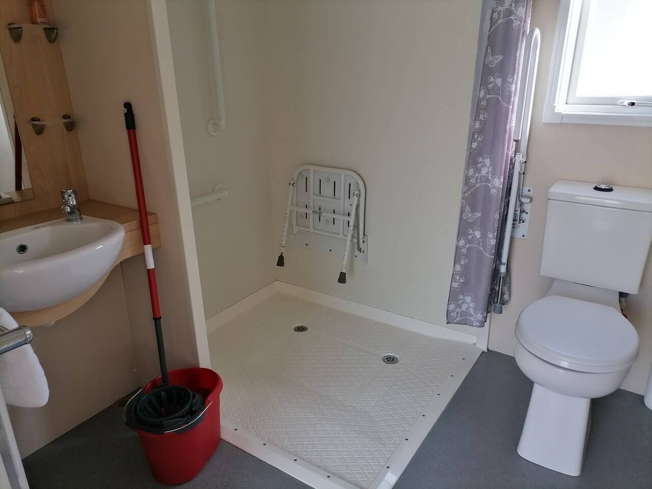 Een kleine badkamer met een wastafel, toilet en douche, plus een rode emmer.