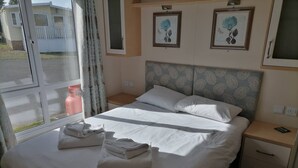 Un lit bien fait, avec du linge de lit et des serviettes blanches, une tête de lit à motifs et une table de chevet avec un téléphone.