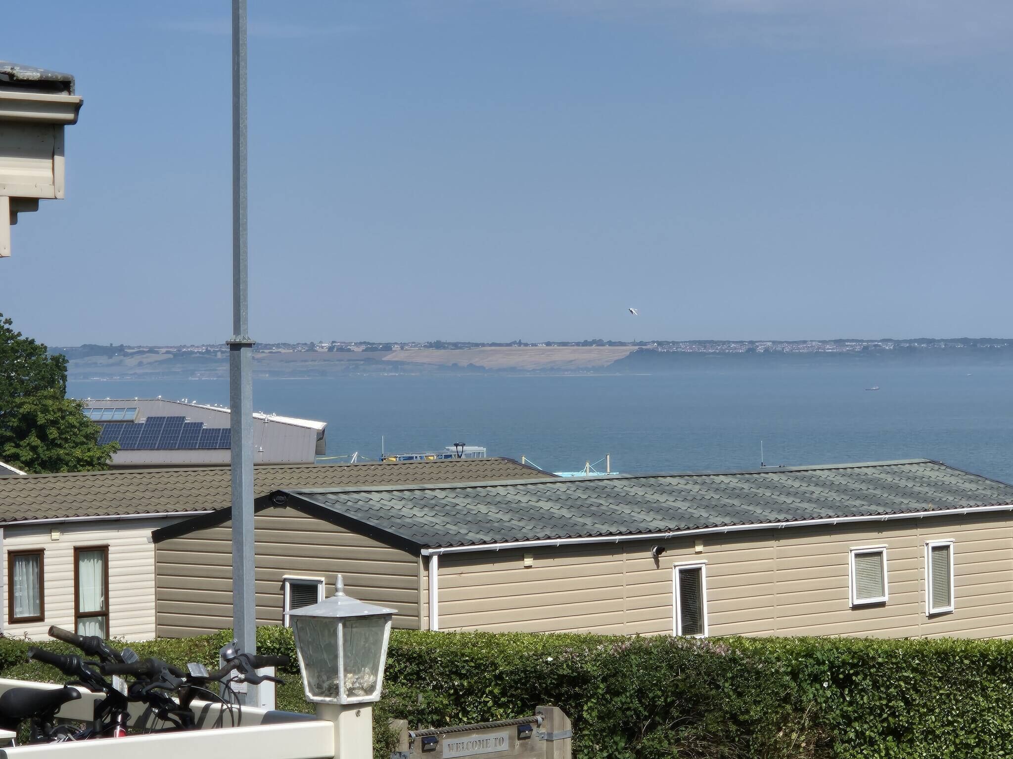 Une vue sur la côte, avec un ciel dégagé, une plage au loin et une rangée de maisons mobiles équipées de panneaux solaires.