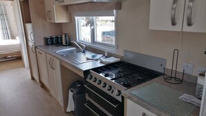 Une cuisine de taille réduite, équipée d’une cuisinière à gaz, d’un évier et d’une fenêtre donnant sur l’extérieur.