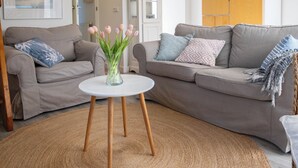 A living room with two grey sofas, a white coffee table, and a vase with pink flowers. - Seagull. (Egmond aan Zee)