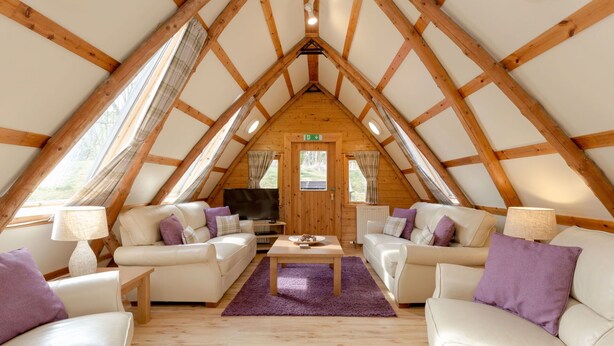 A cozy, well-lit attic room with a pitched wooden ceiling, two white leather sofas, a coffee table, and a television. - Beautiful private villa for 16 guests with WIFI, TV, patio, pets allowed and panoramic view (Ayr)