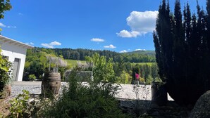 Une vue d’un bâtiment doté d’un mur en pierre et d’un jardin agrémenté de diverses plantes et d’un grand arbre.