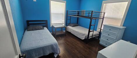 A room with a bunk bed, a single bed, a dresser, and a ceiling fan.