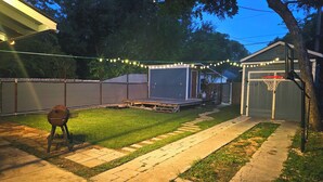 A backyard with a wooden deck, a barbecue grill, a basketball hoop, and a covered playhouse.