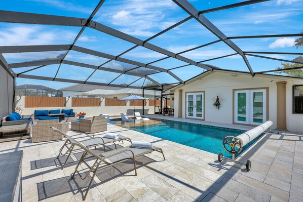 Un espace extérieur abrité avec une piscine, des chaises longues, une table et un parasol au bord de la piscine.