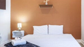 Habitación de hotel con cama, mesita de noche con lámpara, estante con adorno y televisor montado en la pared.