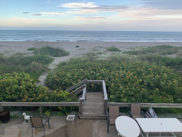 A wooden staircase leading to a beach with a view of the ocean. There are outdoor seating areas with chairs and a table. - Beach Condo - Less than 75 steps from door to sand! (Cocoa Beach)