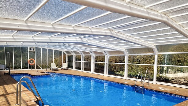 Une piscine couverte avec des parois en verre transparent, une bouée de sauvetage et un escalier pour piscine.