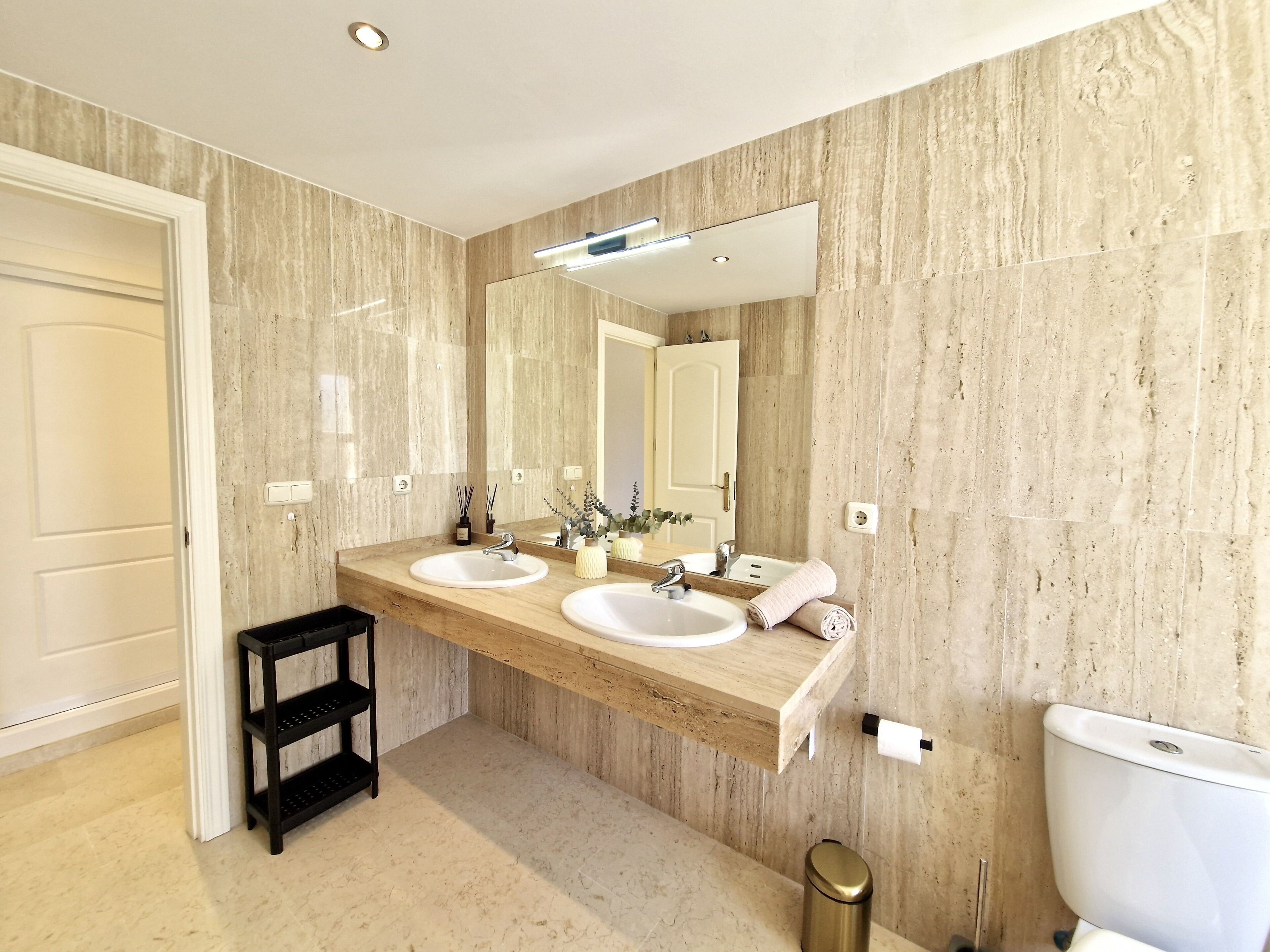 A modern bathroom with two sinks, a large mirror, and a black shelf.