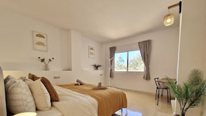 Une chambre moderne avec un lit, une table de chevet, une lampe, une fenêtre, des rideaux et une petite table avec des chaises.