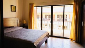 Une chambre d’hôtel comprenant un lit, une table de chevet, une lampe et une grande porte-fenêtre coulissante donnant sur un balcon.